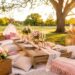 Boho-style picnic rental setup in a sunlit park with low wooden table, layered rugs, cushions, floral arrangements, candles, and styled tableware, creating a fully decorated outdoor picnic experience ready for guests.
